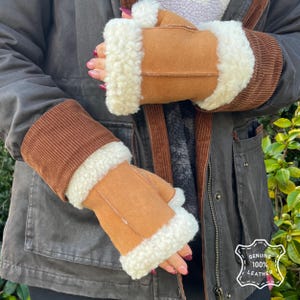 Puede incluir: Guantes sin dedos de cuero marrón con ribete de borrego blanco. Los guantes tienen un puño de pana y están etiquetados como "GENUINE 100% LEATHER".