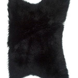 May include: A black sheepskin rug with a soft, fluffy texture. The rug is shaped like a diamond and has a natural, irregular edge.