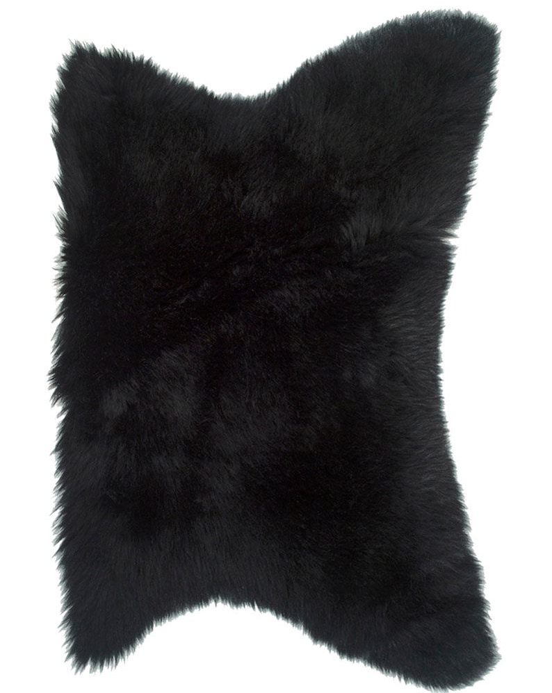 May include: A black sheepskin rug with a soft, fluffy texture. The rug is shaped like a diamond and has a natural, irregular edge.