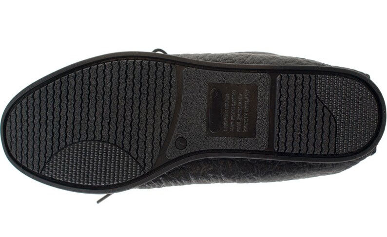 Op de afbeelding: Zwarte leren platte schoenen met een textuurzool en een label aan de zijkant met de tekst "California  Made in China  Leather Upper  Man Made Sole".