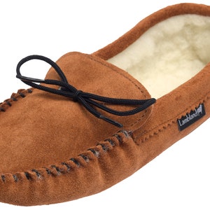 May include: Brown suede moccasin slippers with a black elastic tie and a sheepskin lining. The slippers have a  "Lambland" logo on the side.