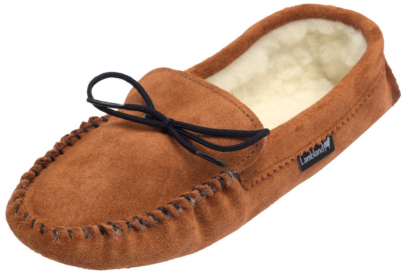 May include: Brown suede moccasin slippers with a black elastic tie and a sheepskin lining. The slippers have a  "Lambland" logo on the side.
