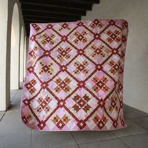 May include: A pink and brown quilt with a diamond pattern. The quilt is made of various fabrics and has a white background.