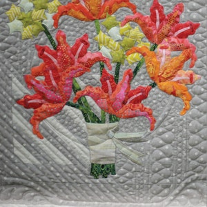 Puede incluir: Un bloque de acolchado con un ramo de lirios y hortensias de color naranja, rojo y rosa. El bloque mide 18 pulgadas por 18 pulgadas y forma parte del patrón de acolchado 16th and Baltimore. El bloque está etiquetado como "ECQ 16B02".