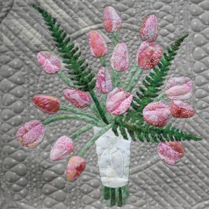 May include: A quilt block featuring a bouquet of pink tulips and green ferns in a white vase. The block is titled "Tulips and Ferns" and is 18 inches by 18 inches.