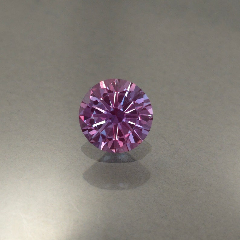 May include: A round, faceted gemstone with a purple and blue color gradient. The gemstone has a star-like pattern in the center.