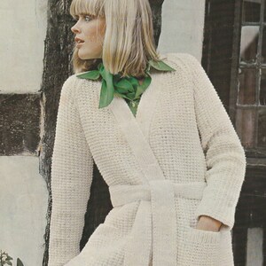 以下が含まれることがあります： 長いオープンフロントとマッチするベルトが付いた白いニットカーディガン。カーディガンはテクスチャのあるステッチパターンと左側に1つのポケットがあります。