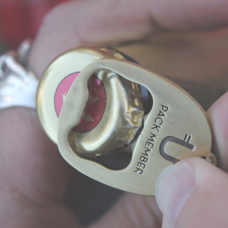 May include: A gold bottle opener with the text "PACK MEMBER" and a stylised "U" with a euro symbol. The opener is attached to a bottle cap.