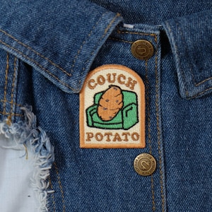 May include: An embroidered patch in beige and green with the text "Couch Potato" and a cartoon image of a potato sitting on a sofa.