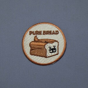 May include: A white and brown embroidered patch with a cartoon bread loaf with a face and the text "PURE BREAD".