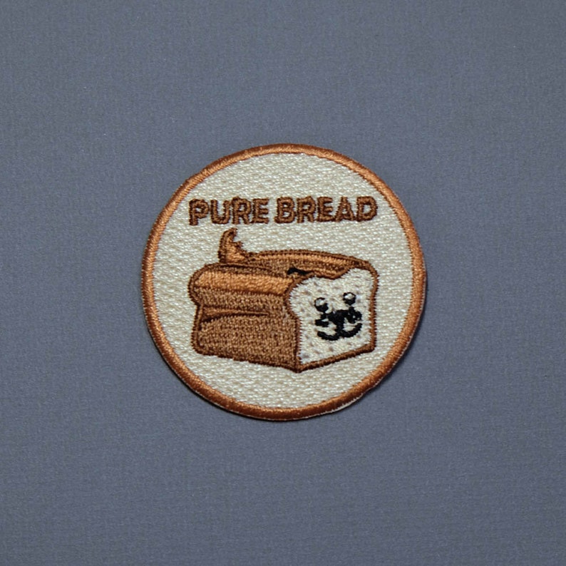 May include: A white and brown embroidered patch with a cartoon bread loaf with a face and the text "PURE BREAD".