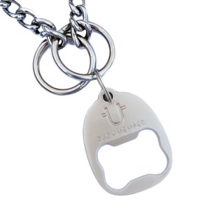 May include: Silver dog chain with a silver bottle opener attached. The bottle opener has a bone-shaped opening and the text "PACK MEMBER" is engraved on the back.