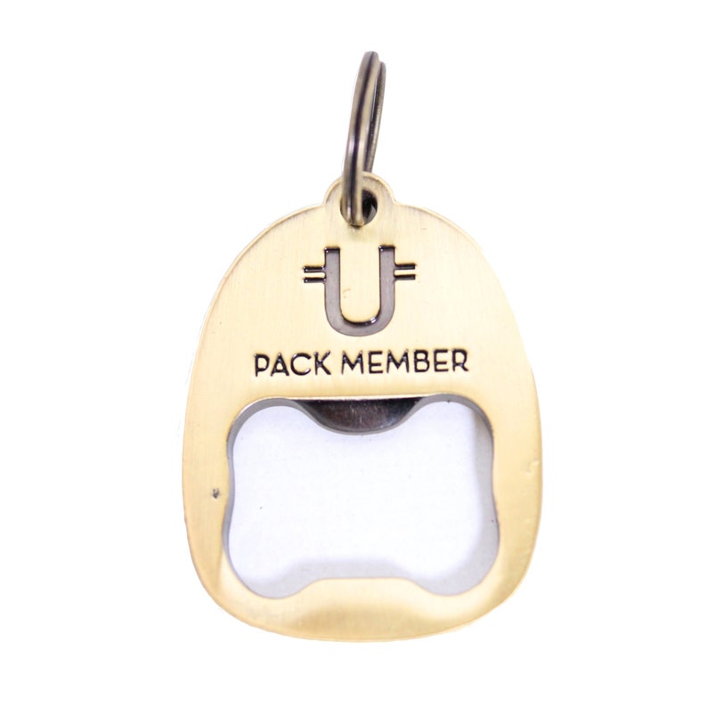 May include: Gold-coloured metal bottle opener keychain with a bone-shaped opening. The keychain has a ring at the top and the words "PACK MEMBER" and "U" engraved on the front.