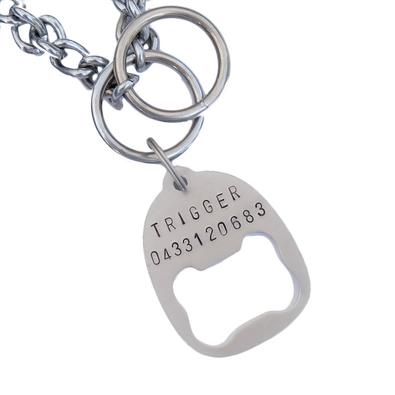 May include: Silver dog tag with a bottle opener attached. The tag is engraved with the text "TRIGGER 0433120683".