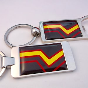 May include: A silver bottle opener keychain with a black, red, and yellow chevron design. The keychain has a ring for attaching to keys.