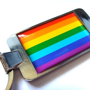 May include: A silver key chain featuring a rainbow flag design. The flag is made of enamel and displays the colours red, orange, yellow, green, blue, indigo, and violet.