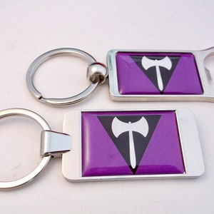 May include: Two silver keychains with a purple and black lesbian pride flag design. The flag features a white axe in a black triangle on a purple background. One keychain has a bottle opener attached.