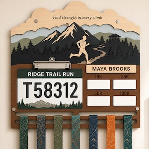 May include: A wooden wall-mounted medal display rack featuring a mountain landscape, a runner silhouette, and the text "Find strength in every climb". It includes a clip for a race bib, a name plate for "MAYA BROOKS", and slots for 10K, 25K, 50K, and 100K race markers with seven hanging medals.
