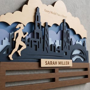 May include: A layered wooden medal display rack featuring a silhouette of a runner and a city skyline. The top section includes the text "Every Medal Has a Story!" and a nameplate with "SARAH MILLER" in dark wood with light wood accents.