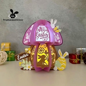 May include: A pink and white papercraft Easter egg with a mushroom-shaped top. The egg is decorated with flowers, bunnies, and the words "Happy Easter".