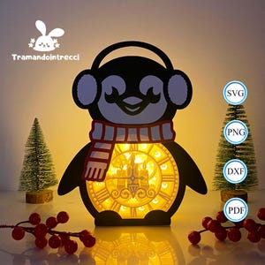 Può includere: Una luce a forma di pinguino in bianco e nero con un design a quadrante d'orologio. Il pinguino indossa paraorecchie e una sciarpa rossa e bianca. Il quadrante dell'orologio si illumina con un bagliore caldo. Sono presenti anche piccoli alberi di Natale e bacche.