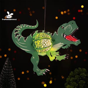 Peut inclure: Une lanterne en papier en forme de dinosaure verte avec une lumière incandescente à l'intérieur. La lanterne est suspendue à une ficelle et présente un design détaillé.