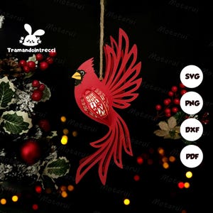 May include: A red cardinal bird ornament with intricate cut-out details, hanging from a twine string. The bird has a yellow beak and is set against a dark background. The image includes the text "Tramandointrecci" and icons for SVG, PNG, DXF, and PDF files.