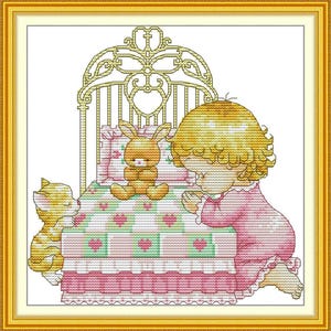 May include: A girl in a pink nightgown kneels beside a bed with a white and pink patterned comforter. A small brown bunny and a yellow cat are on the bed. The bed has a gold metal headboard with a decorative design.