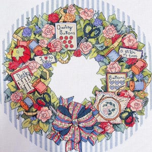 May include: A colorful wreath design featuring sewing-related items like needles, scissors, spools of thread, and buttons. The wreath is adorned with roses and leaves, with text that reads "Quality Buttons", "I love to sew", and "a stitch in time".