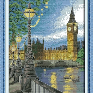May include: A cross-stitch pattern of a night scene in London, England. The image features Big Ben, a bridge, and streetlights. The river Thames is in the foreground with two swans swimming in the water.