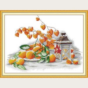 Könnte beinhalten: Kreuzstich-Kunstwerk mit einem Stillleben mit Orangen, orangefarbenen Lampionfrüchten und einer dekorativen Laterne. Die Orangen liegen auf einem weißen Teller und sind von einem goldenen Rahmen umgeben. Das Kunstwerk hat ein Winterthema.
