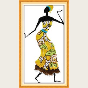 Può includere: Opera d'arte a punto croce di una figura silhouette con un abito giallo floreale, accentuato da un turbante e una cintura blu. La figura è incorniciata in una cornice rettangolare dorata, su sfondo bianco.