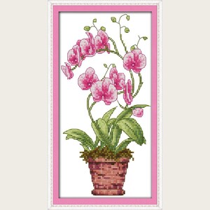 Op de afbeelding: Kruissteekkunstwerk van een roze orchidee in een terracotta pot, omlijst in roze. Het borduurwerk toont gedetailleerde steken van de bloemen, groene bladeren en stelen van de orchidee. Een decoratief bloemenontwerp.