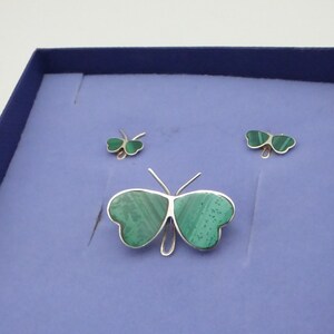 May include: A set of three silver butterfly jewelry pieces with green malachite stone inlays. The set includes a brooch and two earrings.
