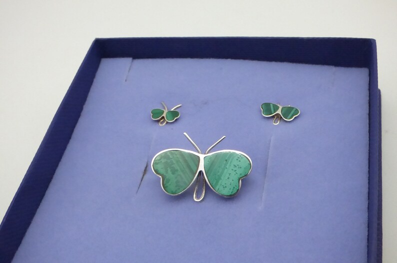 May include: A set of three silver butterfly jewelry pieces with green malachite stone inlays. The set includes a brooch and two earrings.