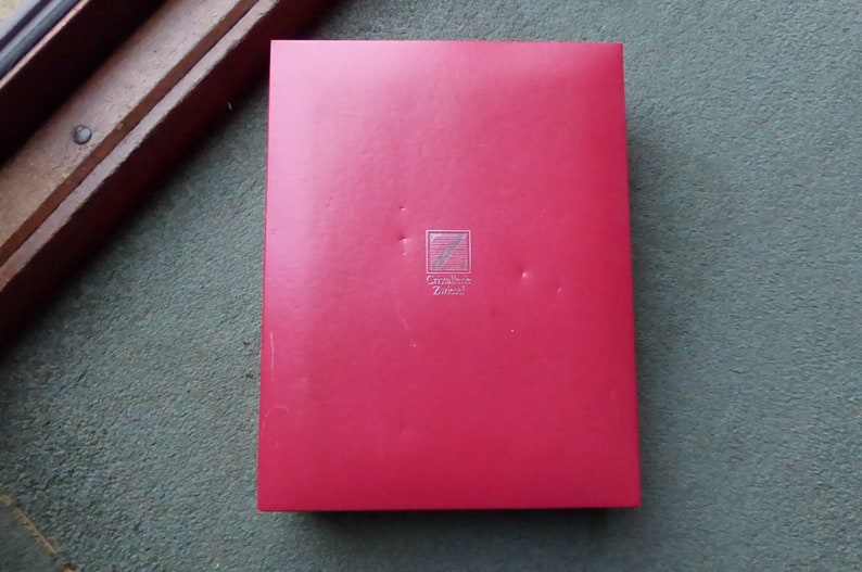 K&ouml;nnte beinhalten: Eine rote Box mit einem silbernen Logo, auf dem "Cr&eacute;ation Z&uuml;ndorf" steht.