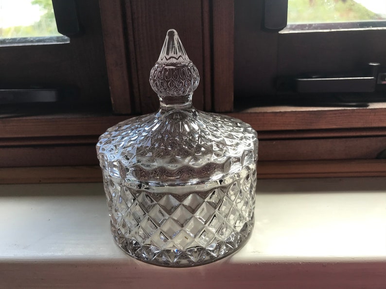 May include: A clear glass jar with a diamond pattern and a clear glass lid with a pointed top.