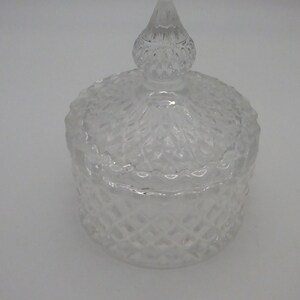 May include: A clear glass jar with a diamond-shaped pattern and a matching lid with a pointed top.