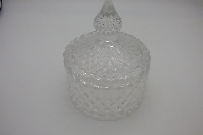 May include: A clear glass jar with a diamond-shaped pattern and a matching lid with a pointed top.