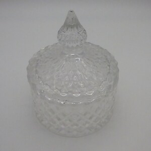 May include: A clear glass jar with a textured diamond pattern and a matching lid. The lid has a pointed top.
