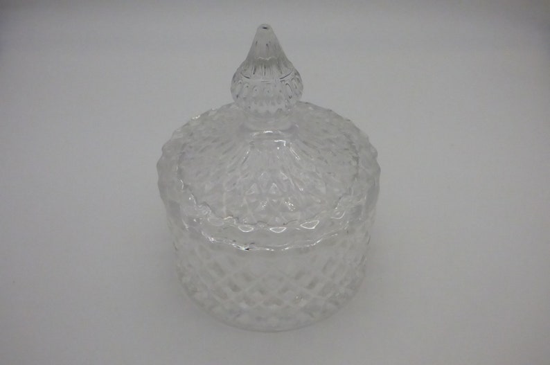 May include: A clear glass jar with a textured diamond pattern and a matching lid. The lid has a pointed top.