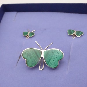 May include: A set of three silver butterfly jewelry pieces with green malachite stone accents. The set includes a brooch and two earrings.