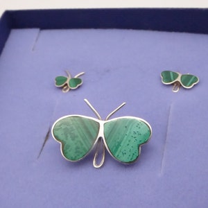 May include: A set of three silver butterfly jewelry pieces with green malachite stone accents. The set includes a brooch and two earrings.
