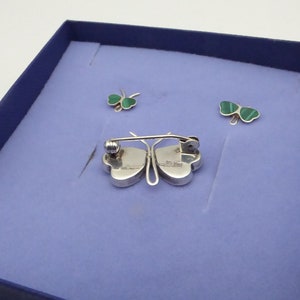 May include: A set of three silver shamrock jewelry pieces in a blue box. The pieces include a brooch and two earrings. The shamrocks are green and have a silver backing.