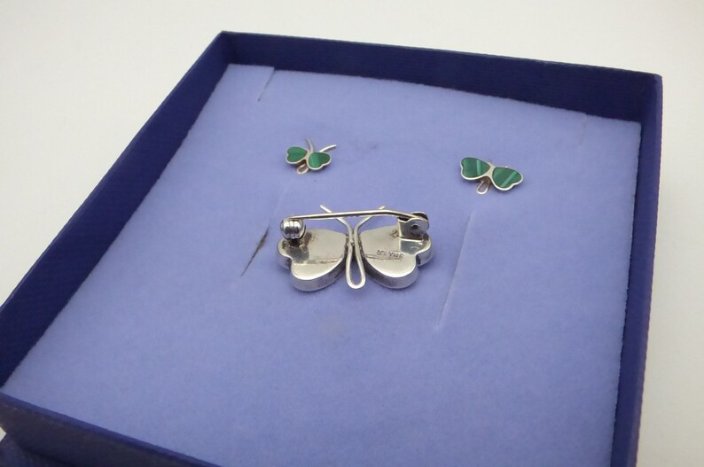 May include: A set of three silver shamrock jewelry pieces in a blue box. The pieces include a brooch and two earrings. The shamrocks are green and have a silver backing.