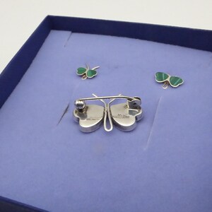 May include: A set of three silver butterfly brooches with green malachite wings. The brooches are displayed in a blue velvet box.