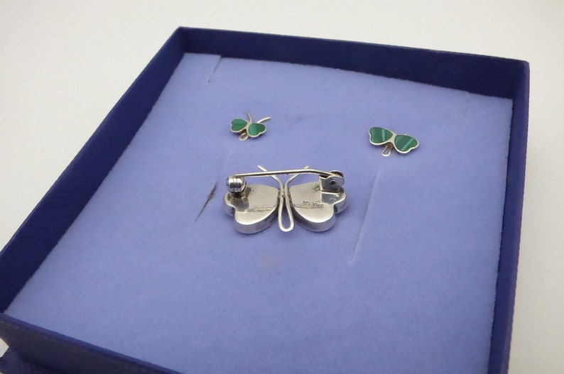 May include: A set of three silver butterfly brooches with green malachite wings. The brooches are displayed in a blue velvet box.