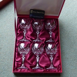 K&ouml;nnte beinhalten: Satz von sechs klaren Kristallweingl&auml;sern in einer mit rotem Samt ausgekleideten Schachtel. Die Schachtel tr&auml;gt ein Etikett mit der Aufschrift "Schon Zwarend Glas".