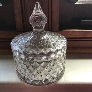 May include: A clear glass jar with a diamond-shaped pattern and a domed lid with a pointed top. The lid is also decorated with a diamond-shaped pattern.