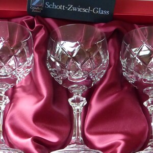 K&ouml;nnte beinhalten: Drei klare Weingl&auml;ser aus Glas mit einem Diamantenmuster auf einem roten Satinuntergrund. Die Gl&auml;ser befinden sich in einer Schachtel mit dem Logo Schott-Zwiesel-Glass.